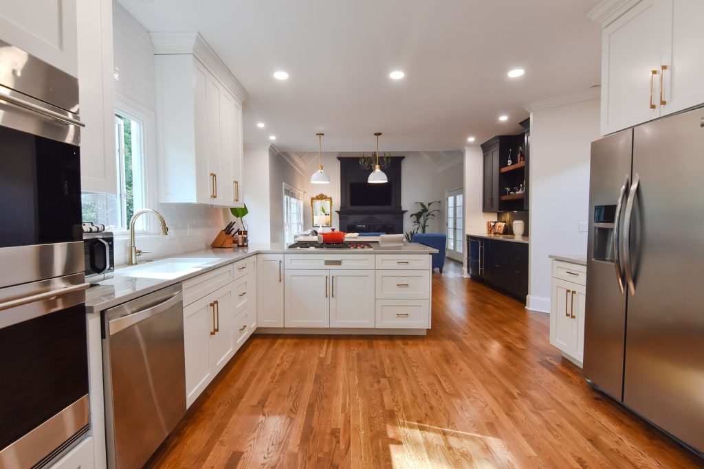 Wide white Alpharetta kitchen with a window over the sink, peninsula cooktop, oak floors, and a dark living-room fireplace beyond.
