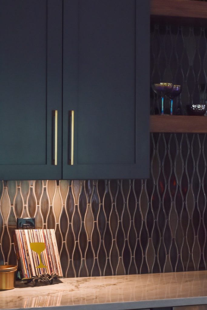 Navy bar cabinetry and iridescent glass tile with coupe glasses and a bowl on a walnut floating shelf in Alpharetta.