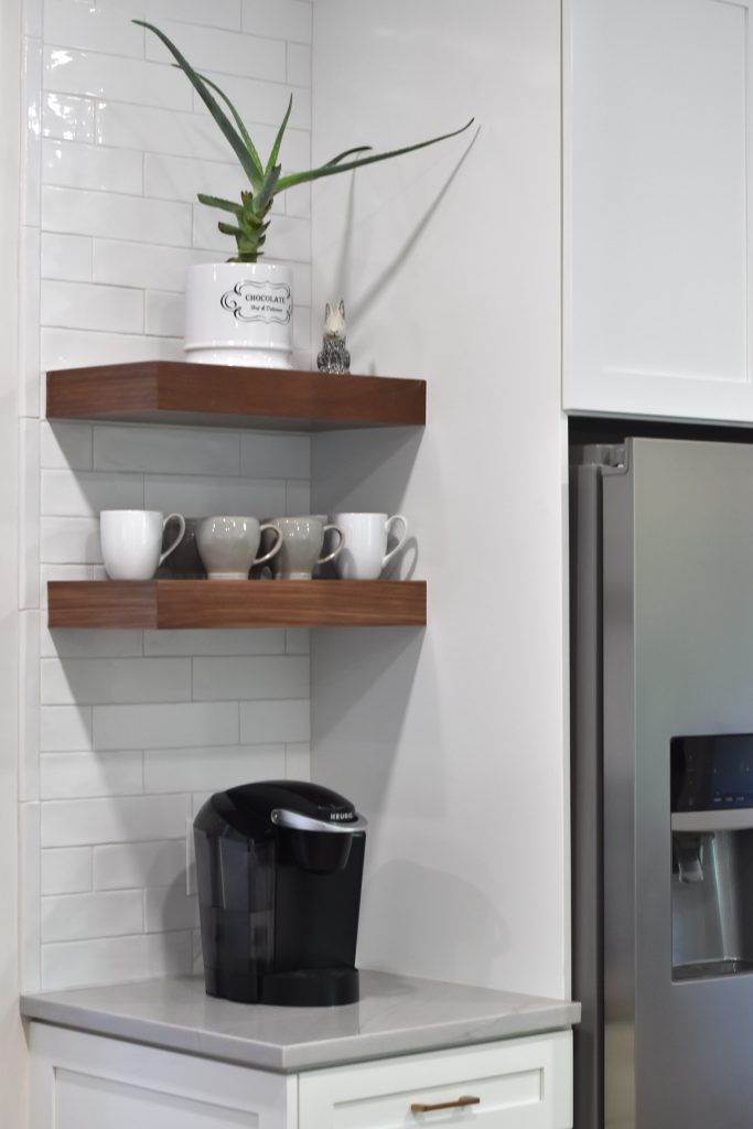 Corner coffee nook with walnut shelves, an aloe plant, mugs, a Keurig, and subway tile beside a stainless refrigerator in Alpharetta.