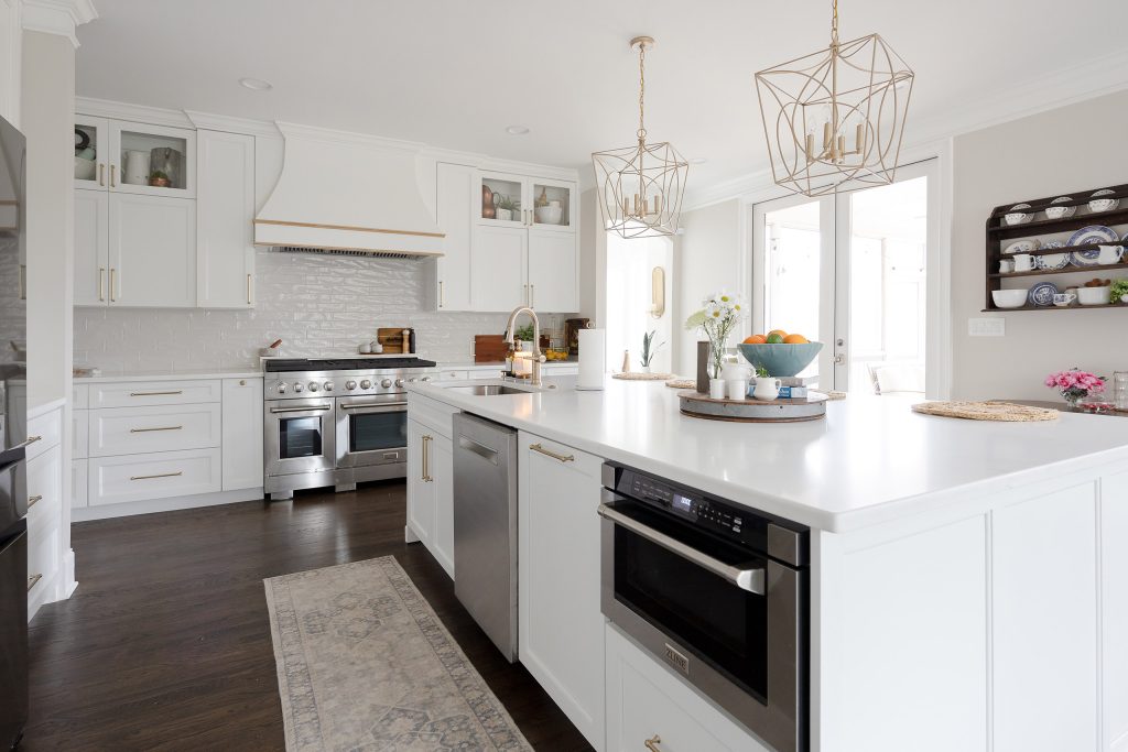 White kitchen with center island, stainless double-oven range, gold cage pendants, and a runner on dark hardwood.