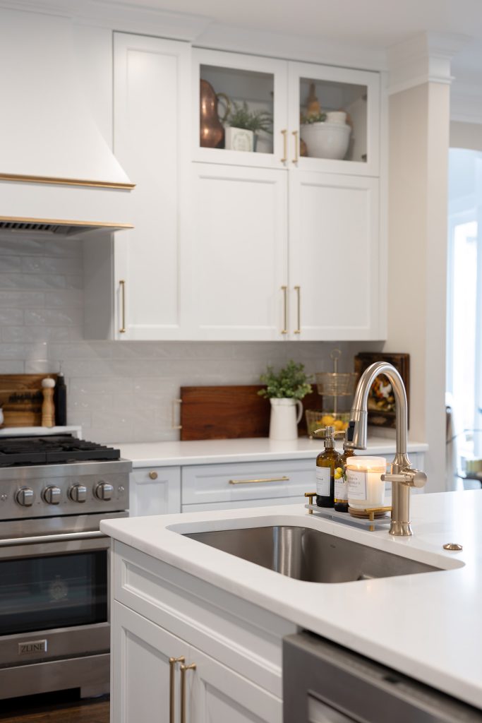 White island with undermount sink, brushed-nickel faucet, glass-front uppers, and a stainless range in the background.