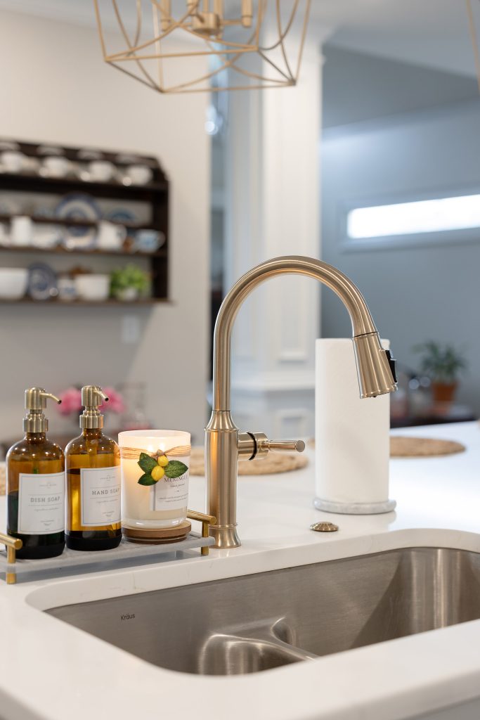 Undermount stainless sink in white quartz island with a brushed-nickel faucet, amber soap bottles, and a lemon candle.