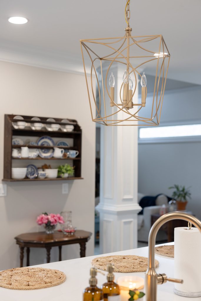 Brushed-gold cage lantern pendant over the island, with a wood hutch of blue-and-white china on the wall behind.