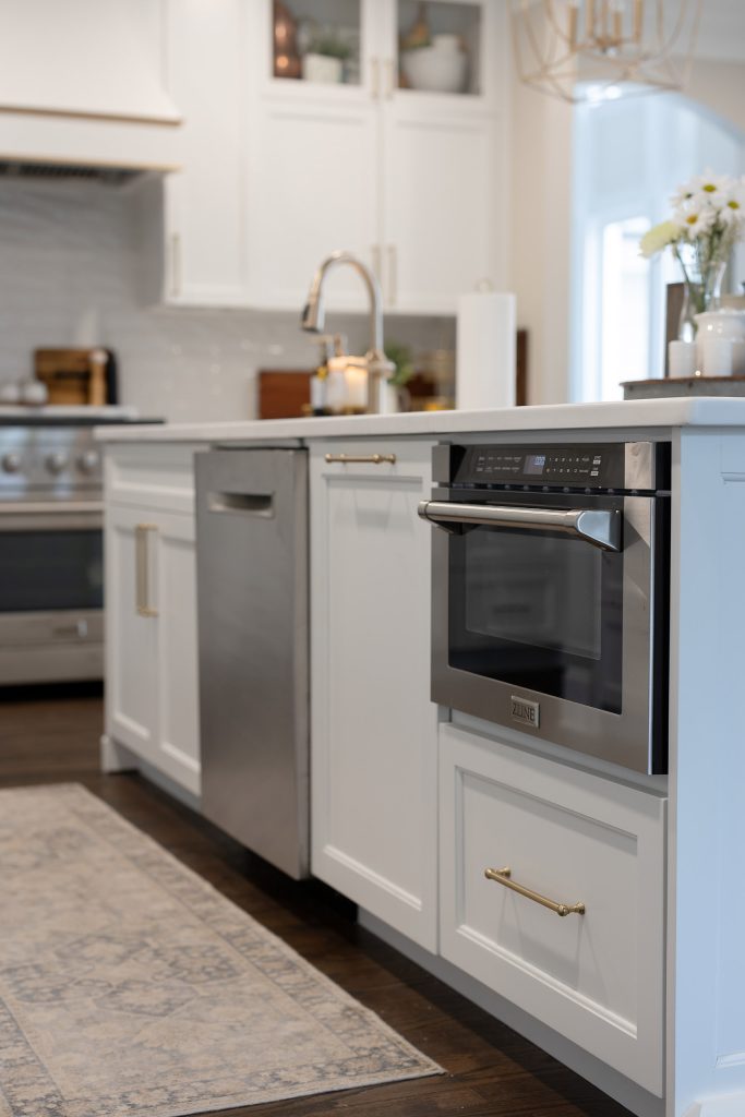 Island with a built-in stainless microwave drawer, dishwasher, brushed-gold pulls, and a runner rug on dark hardwood.
