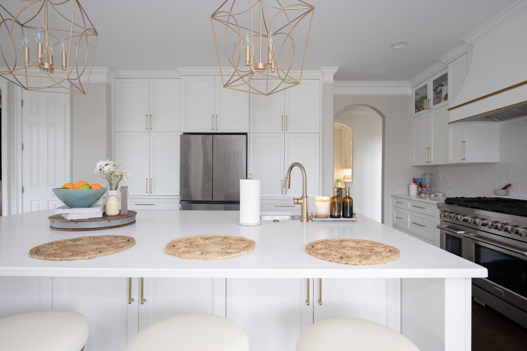 White quartz island with three jute placemats and brushed-gold pulls, stainless fridge and white cabinets behind.