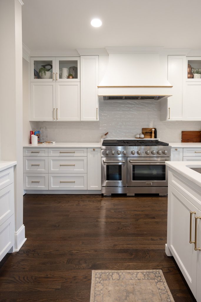 Butler's pantry with a bar sink, gold faucet, built-in wine fridge, open lit shelving, and glossy white tile.