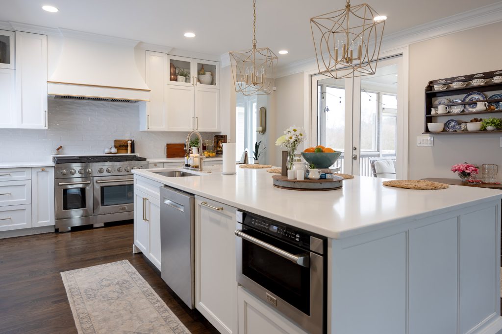 Wide white kitchen island with built-in microwave, gold pendants, French doors, and a blue-and-white china hutch.