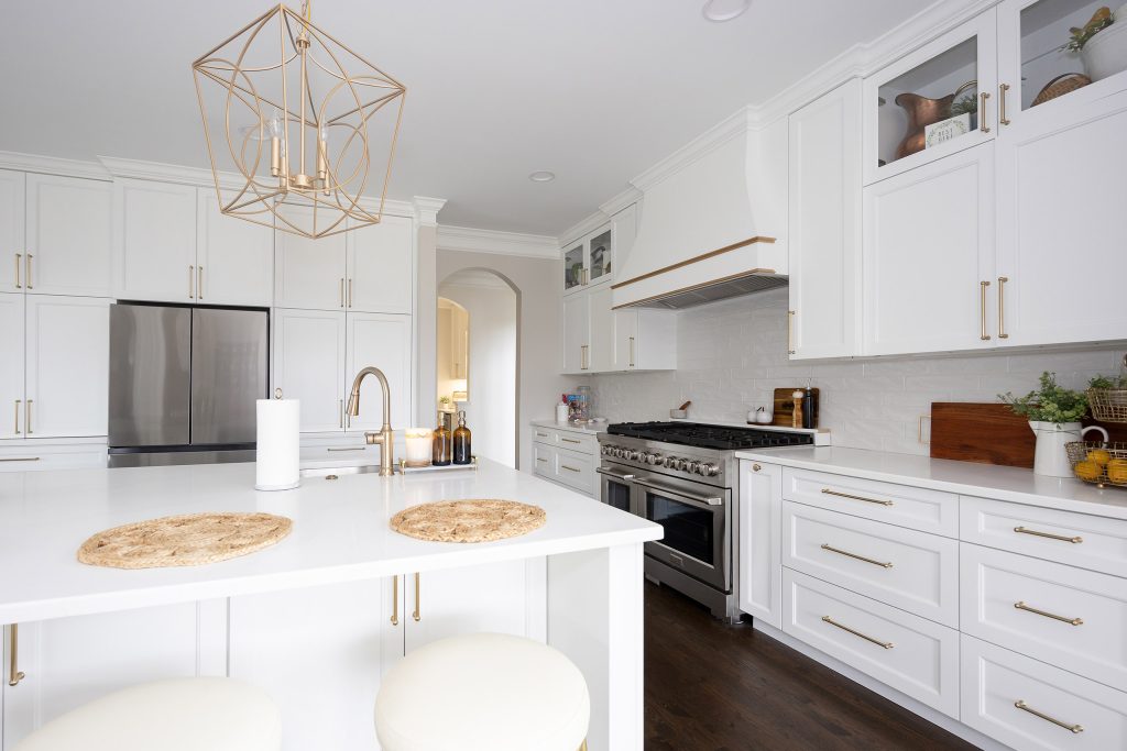 White quartz island with jute placemats and sink, facing a stainless range and gold-trimmed hood on dark hardwood.
