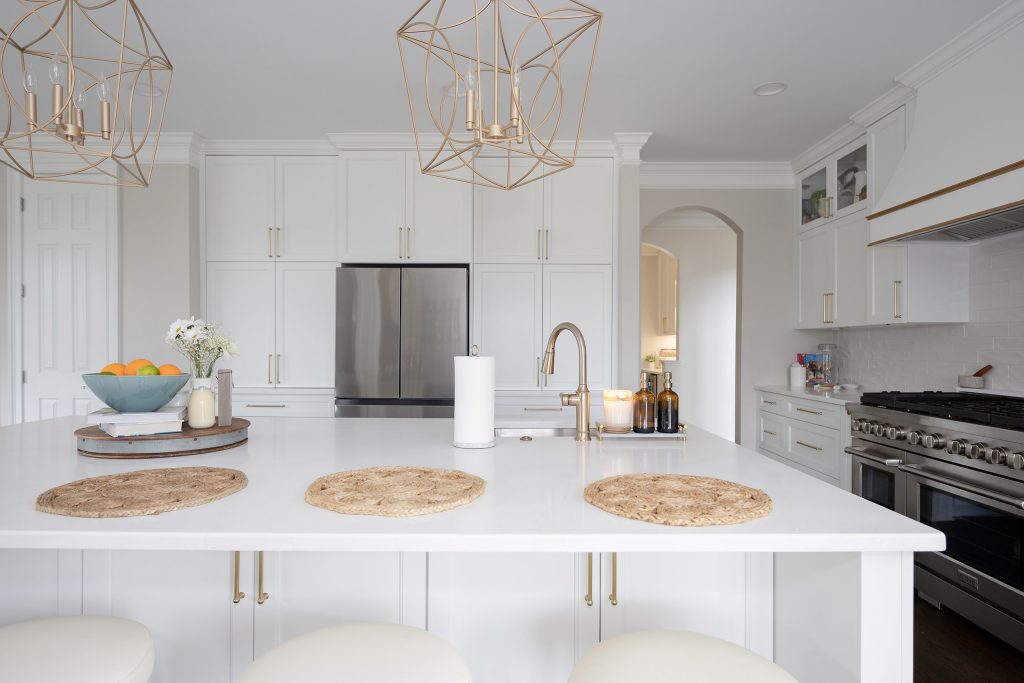 White quartz island with jute placemats and gold pulls, facing a stainless range and refrigerator across dark floors.