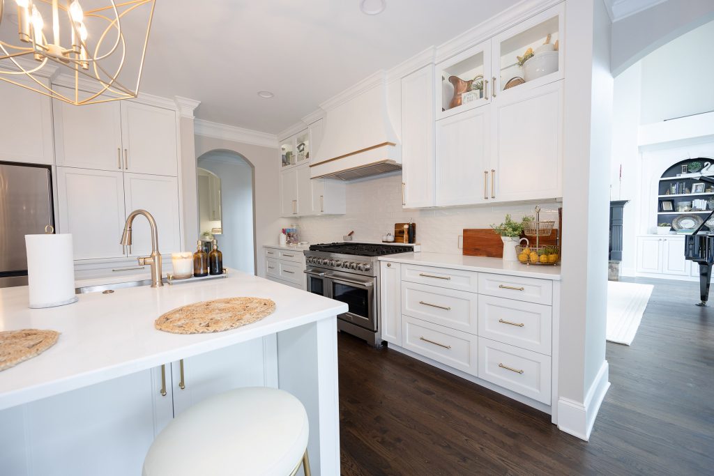 White kitchen island with a cream stool and gold pulls, stainless range, and a view through to a room with a piano.