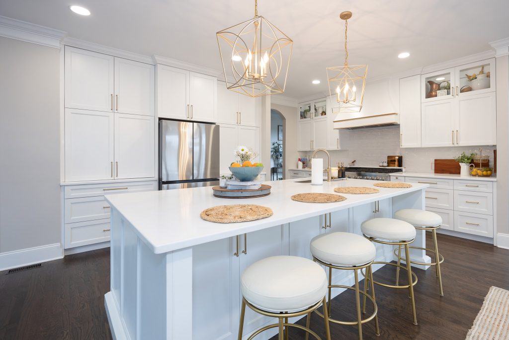 White quartz island with four round gold-legged barstools, jute placemats, and paired gold cage pendants overhead.