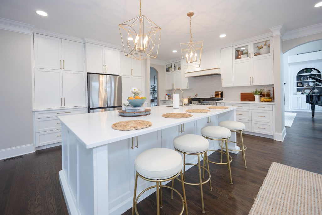 Large white quartz island with round gold-based barstools, jute placemats, and gold cage pendants in a bright kitchen.