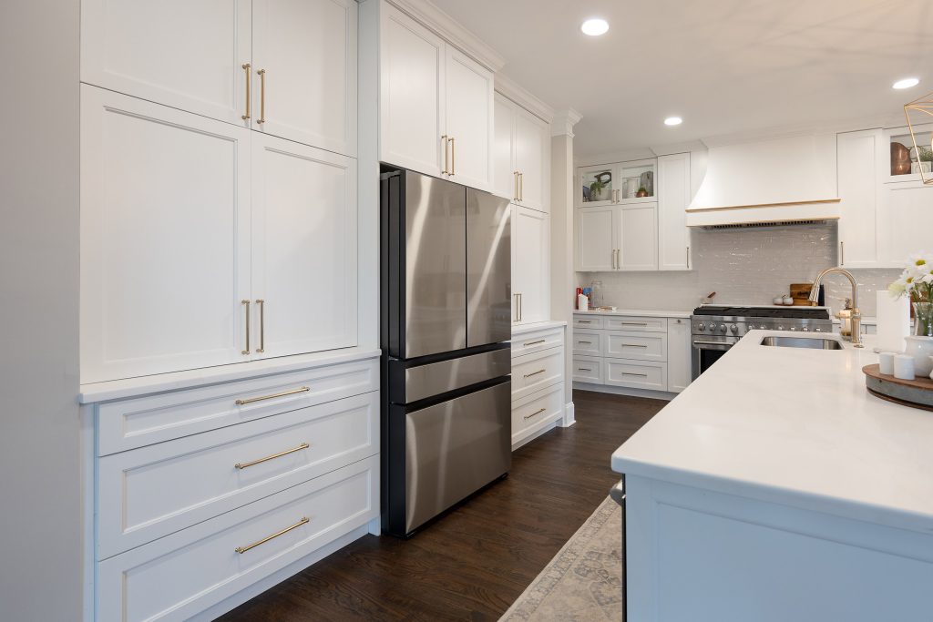 Floor-to-ceiling white cabinets flanking a stainless French-door fridge, with a white quartz island in the foreground.