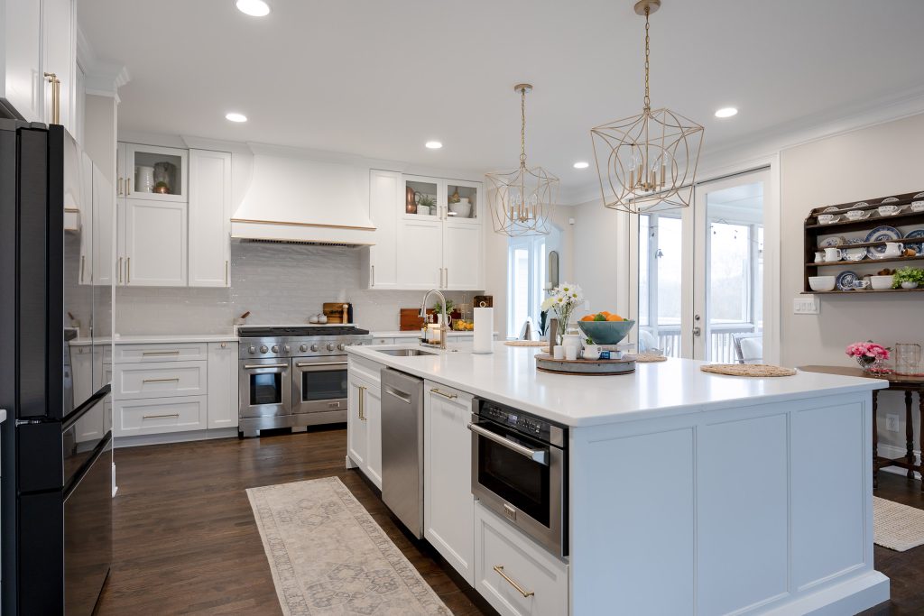 White quartz island with built-in microwave drawer, stainless range, gold pendants, and a runner over dark hardwood.
