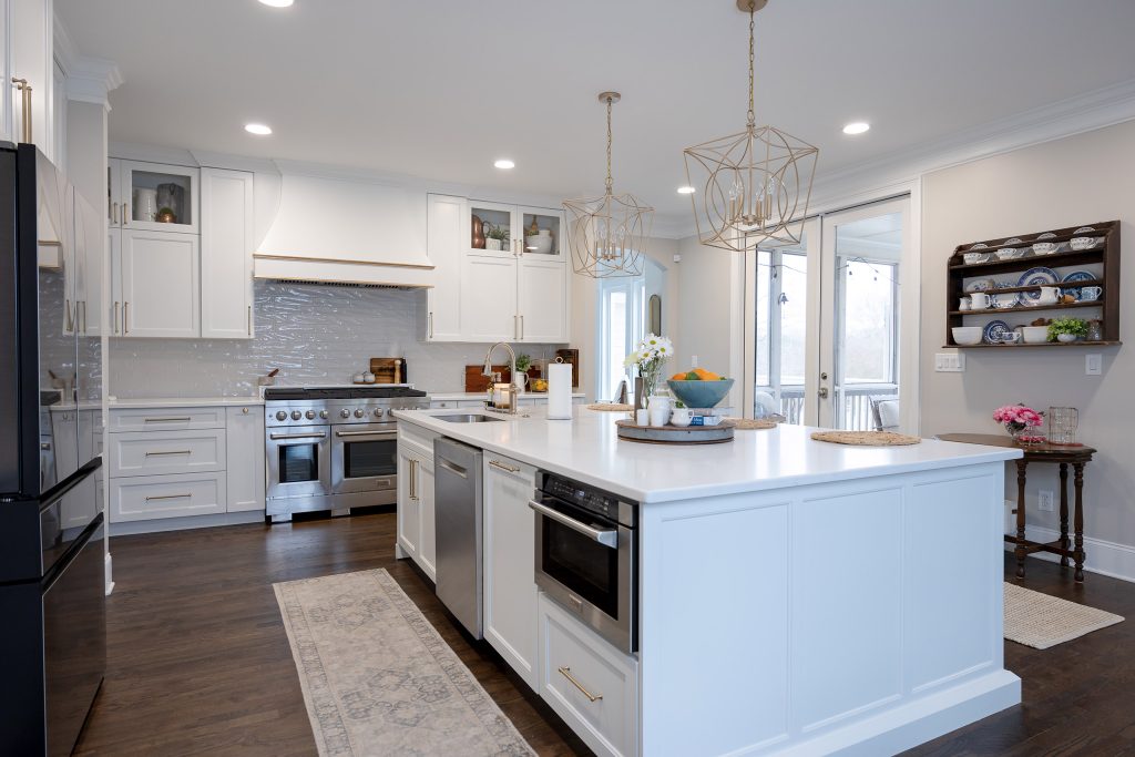 Bright white kitchen with large island, cream-and-gold barstools, black French-door fridge, and gold cage pendants.