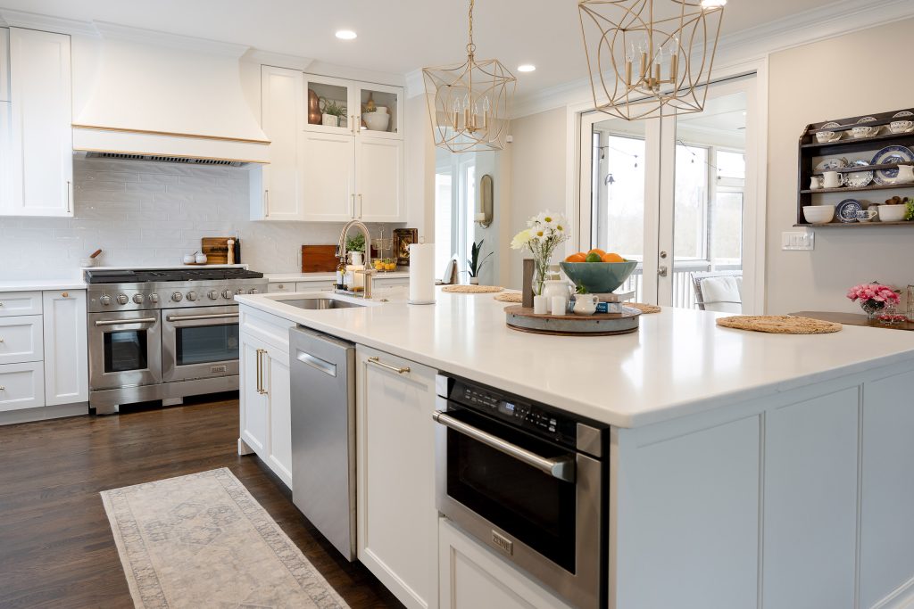 White quartz island with built-in microwave and stainless range beyond, gold pendants, and a blue-and-white china hutch.