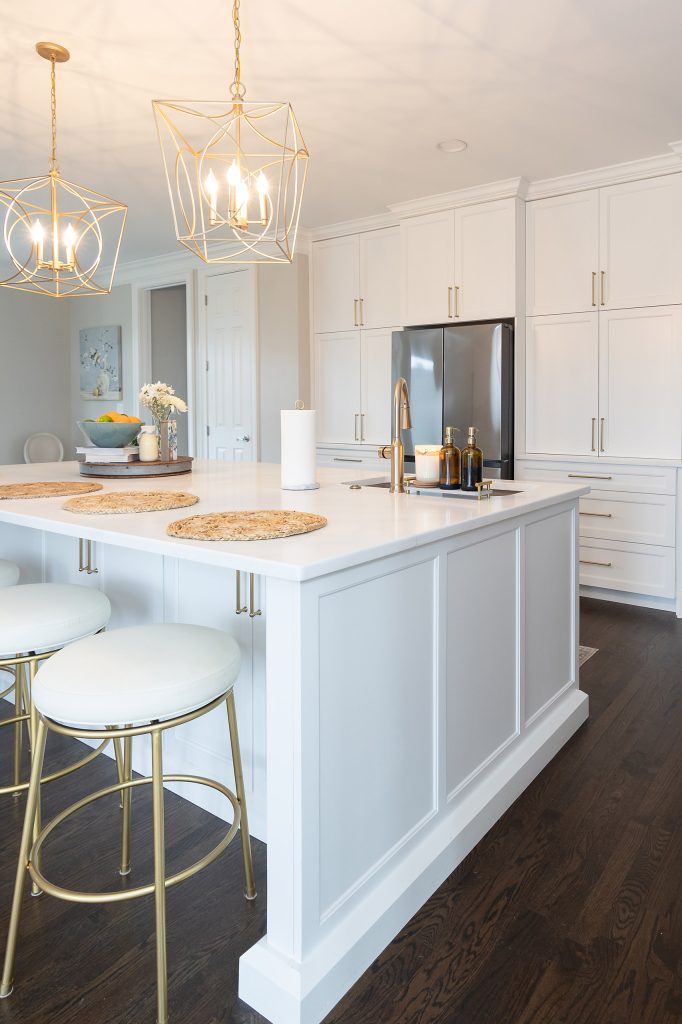 White quartz island with jute placemats, gold-and-cream barstools, and twin gold cage pendants overhead.