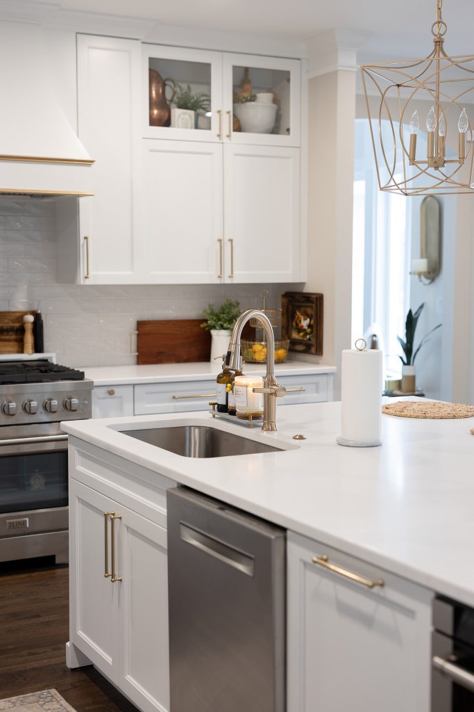 Island prep sink in white quartz with brushed-nickel faucet, gold-pull cabinets, and glass-front display cabinets above.