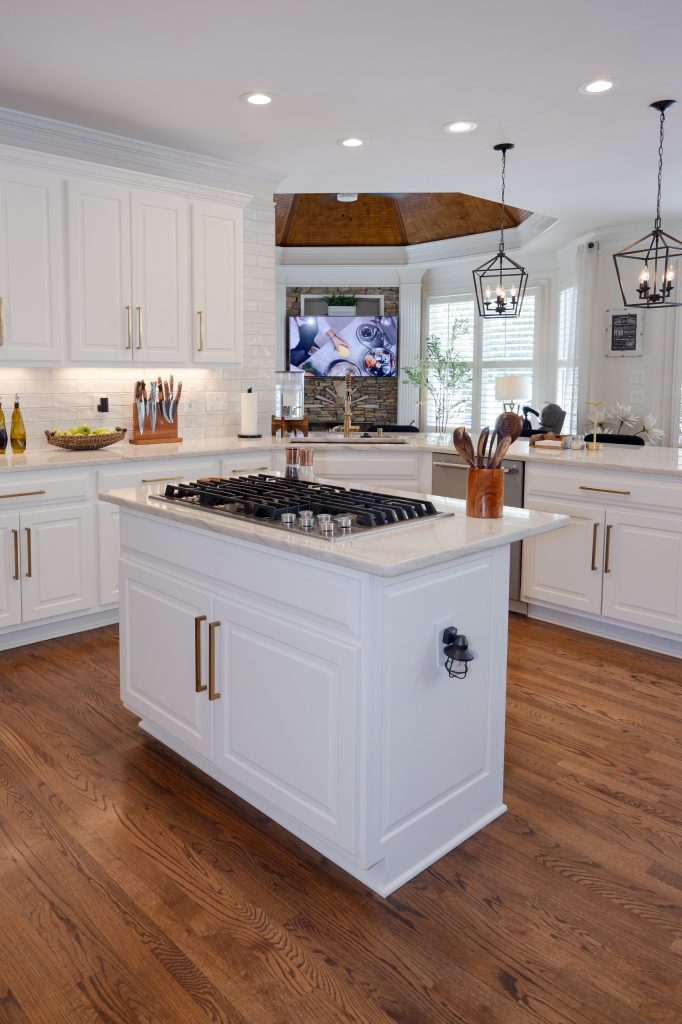 White kitchen with a center island cooktop, marble-look quartz counters, subway tile backsplash, and a wood-clad range hood.
