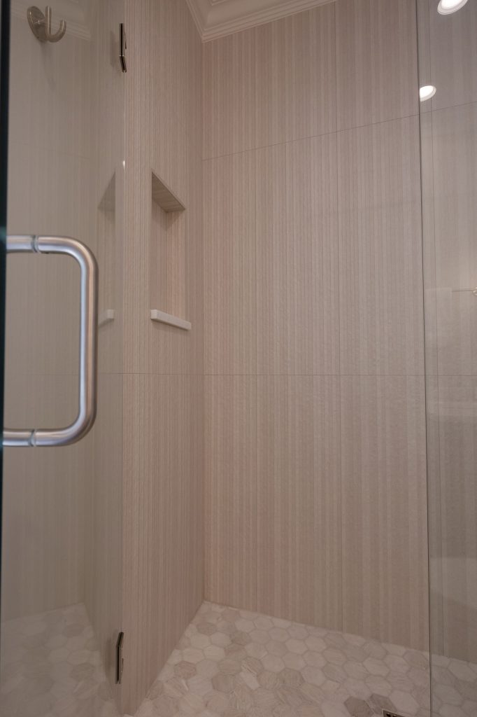 Walk-in shower with vertical linear tile, a recessed niche, and a marble hexagon mosaic floor.
