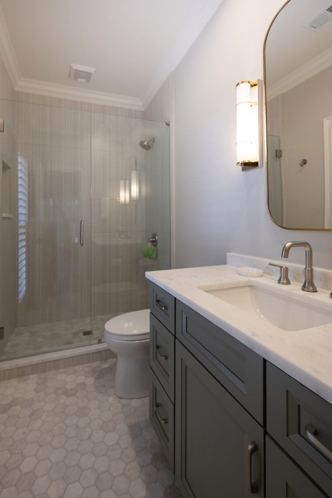 Guest bath with a grey vanity, marble-look top, frameless glass shower, and a marble hex-tile floor.