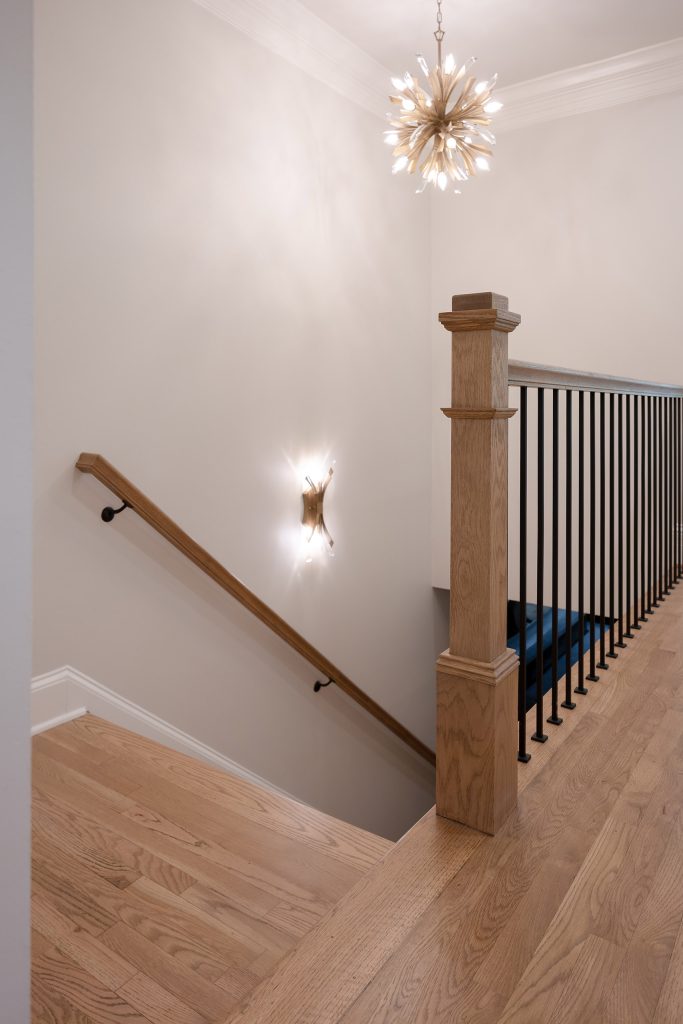 Upstairs landing with a starburst chandelier, stained-oak newel post, iron balusters, and white oak flooring.