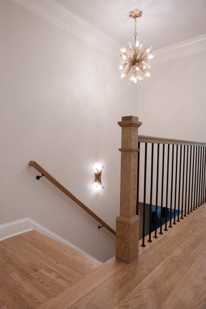 Stair landing with a gold starburst chandelier, wood newel post, black iron balusters, and oak floors.