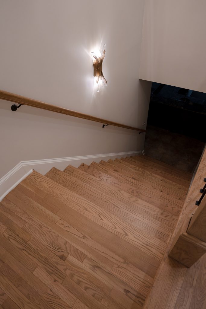 Staircase viewed from above with white oak treads, a wood handrail, and a crystal-and-brass wall sconce.