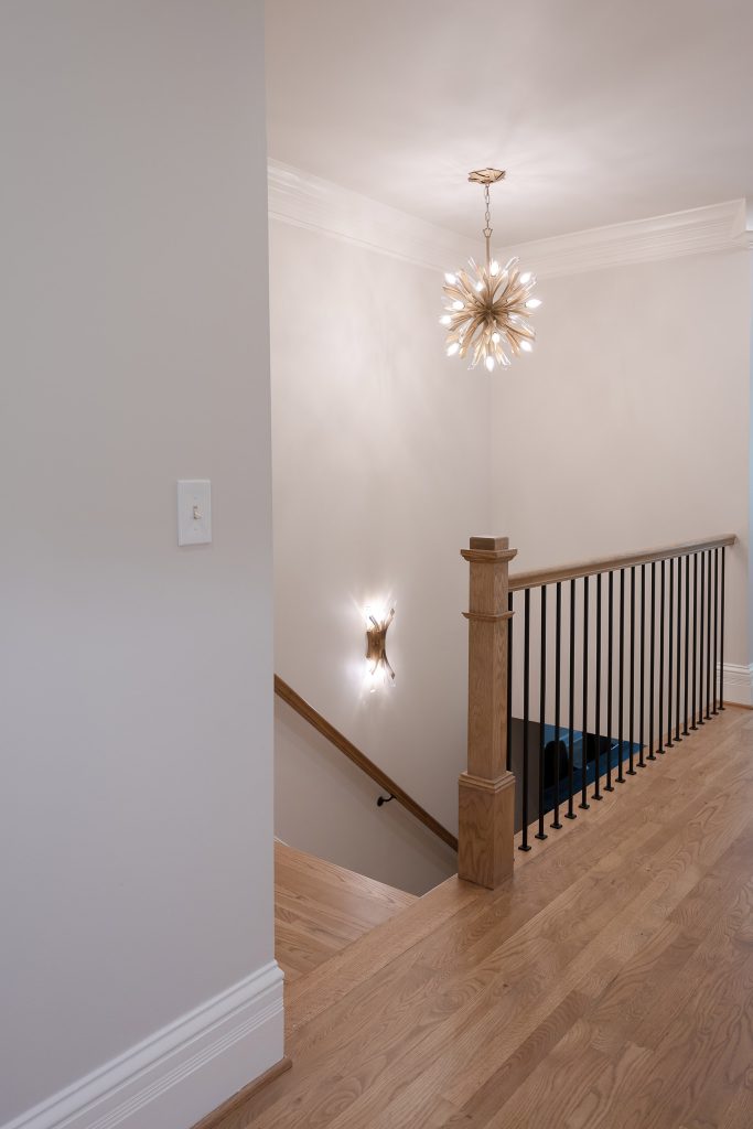 Stair landing with a gold starburst chandelier, oak floors, iron balusters, and a stained-wood newel post.
