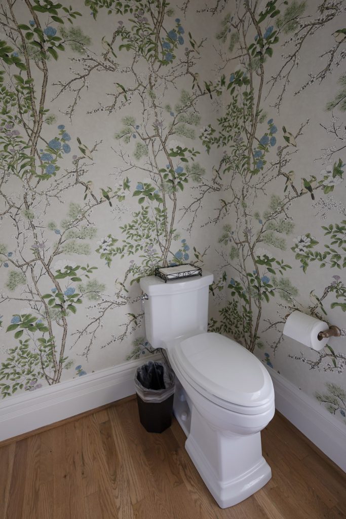 Powder room corner with bird-and-floral chinoiserie wallpaper, a white toilet, and oak flooring.