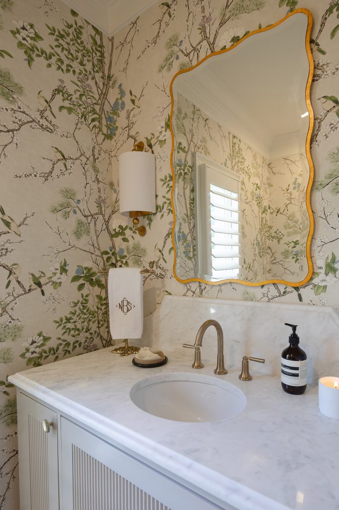 Powder room with green chinoiserie wallpaper, a reeded white vanity, marble top, and a scalloped gold mirror.