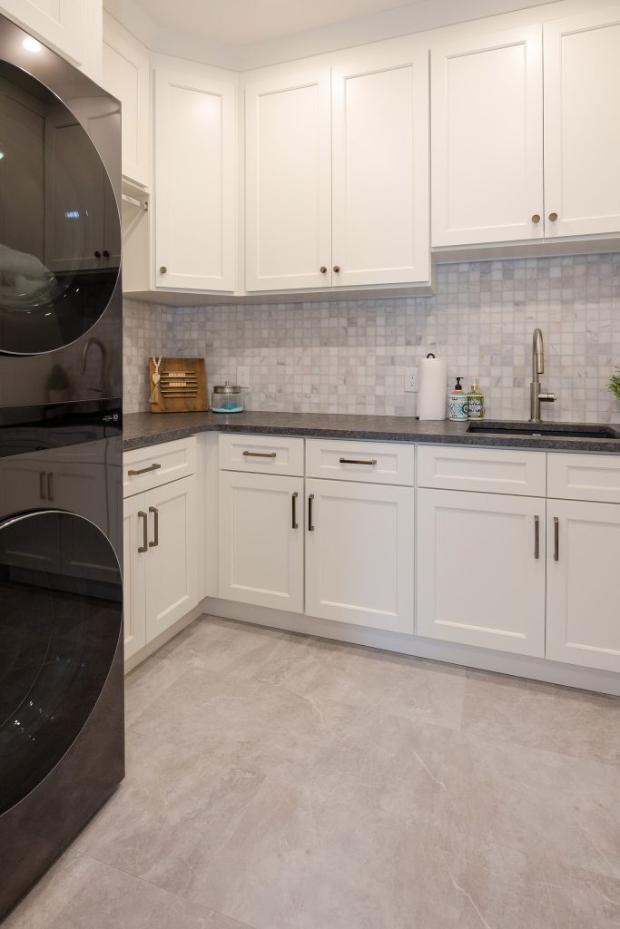 Laundry room with a black stacked washer and dryer, white cabinetry, marble mosaic backsplash, and dark counters.