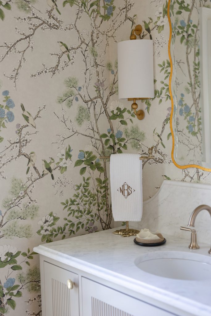 Powder room with bird-and-branch chinoiserie wallpaper, a fluted white vanity, marble top, and gold mirror.
