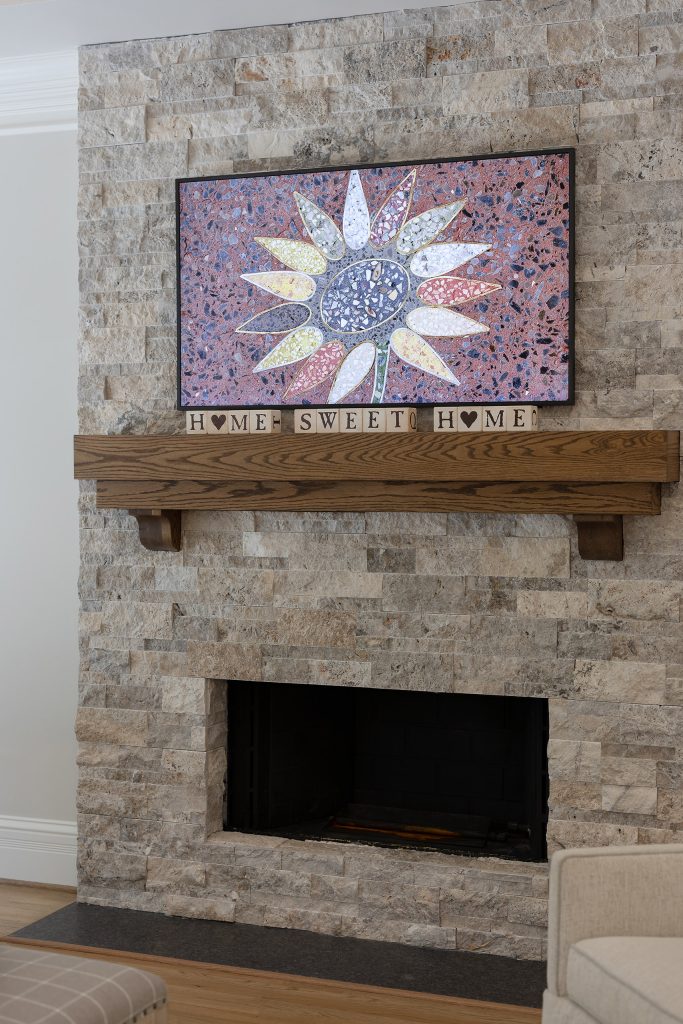 Stacked-stone fireplace with a terrazzo sunflower artwork, stained-oak mantel, and a black granite hearth.