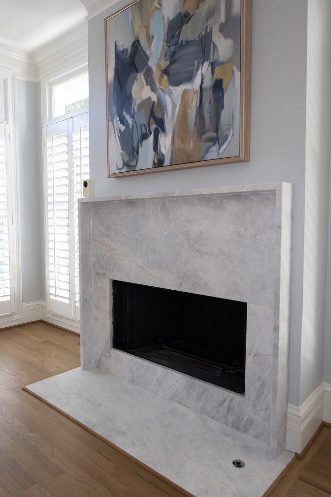 Veined quartzite slab fireplace surround with a blue-and-neutral abstract painting above.