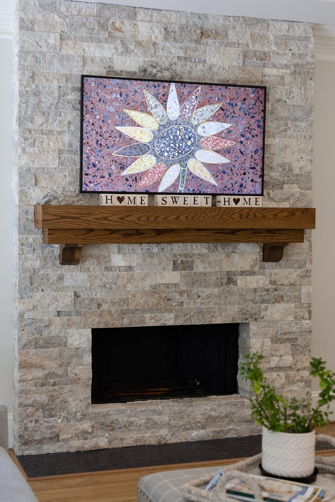 Silver travertine ledgestone fireplace with a terrazzo sunflower panel and 'Home Sweet Home' tiles on the mantel.