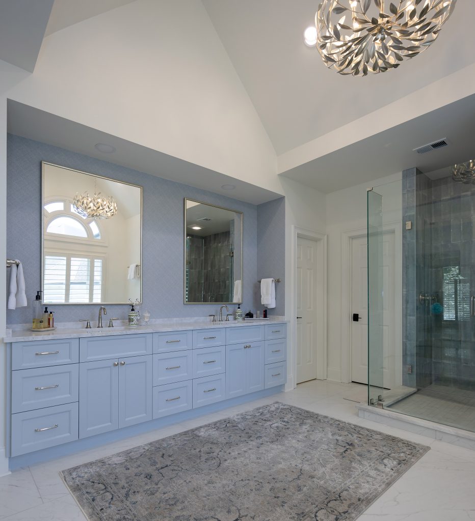 Primary bathroom with a vaulted ceiling, pale blue double vanity, marble countertops, and a glass-enclosed shower in grey stacked tile.
