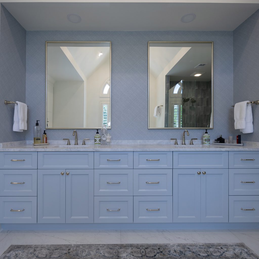 Master bath with a leaf-form chandelier, freestanding tub, arched window, and marble-look floors.