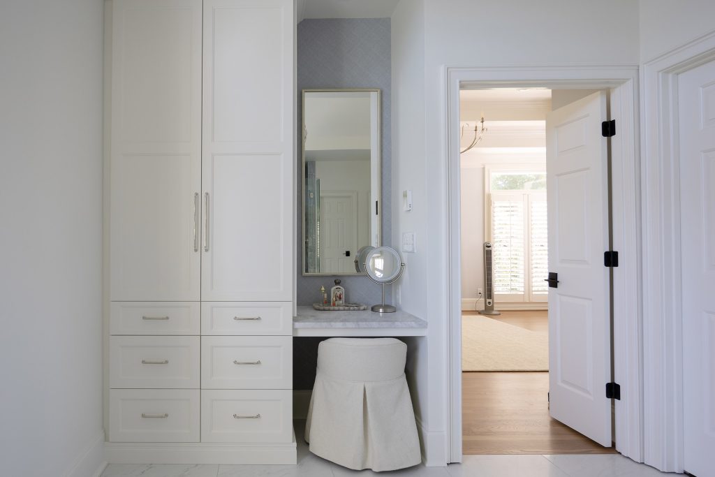 Built-in white vanity nook with a makeup counter, skirted stool, and a doorway to the bedroom.