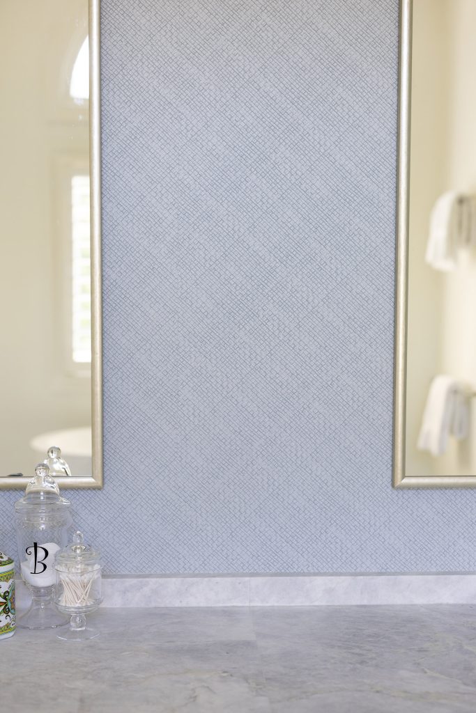 Blue bathroom with textured grasscloth-look walls, a marble base, and a gold-framed mirror.