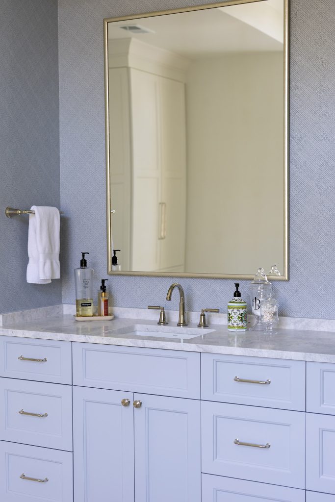 Powder-blue vanity with a marble top, a gold-framed mirror, and blue grasscloth-look walls.