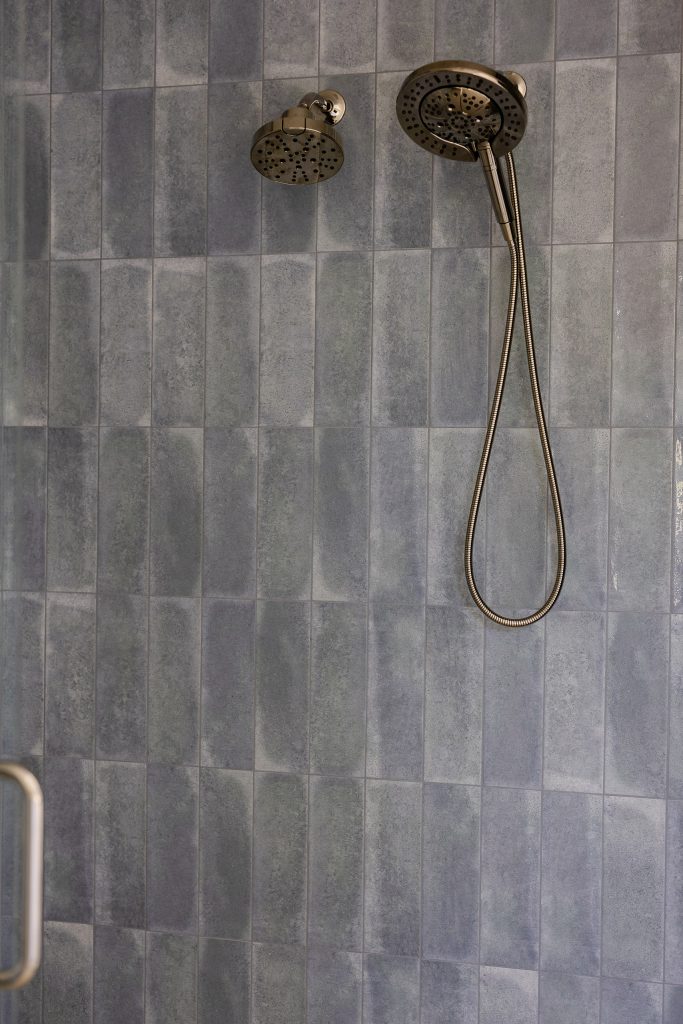 Shower wall in blue zellige-look tile with a fixed rain head and a handheld sprayer on brushed hardware.