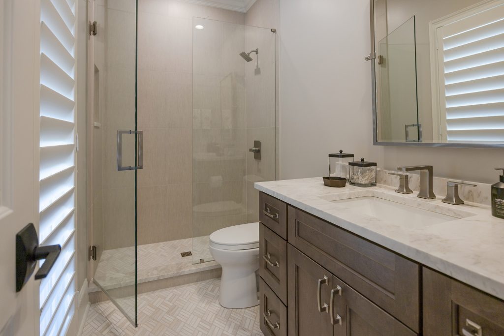 Guest bath with a walk-in glass shower, espresso vanity, marble-look top, and a framed mirror.