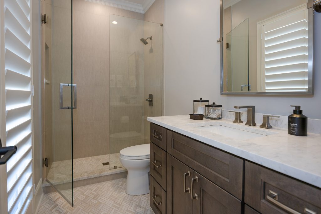 Bathroom with a frameless glass shower, dark vanity, marble-look counter, and plantation shutters.