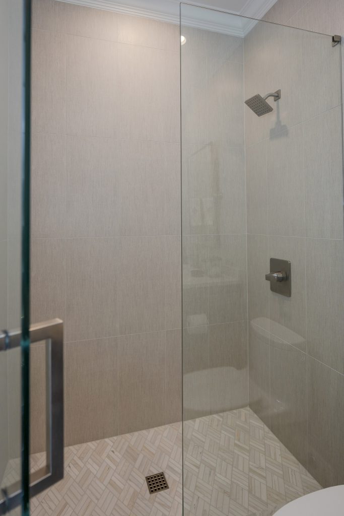 Walk-in shower with vertical greige large-format tile, a square rain head, and a marble herringbone floor.