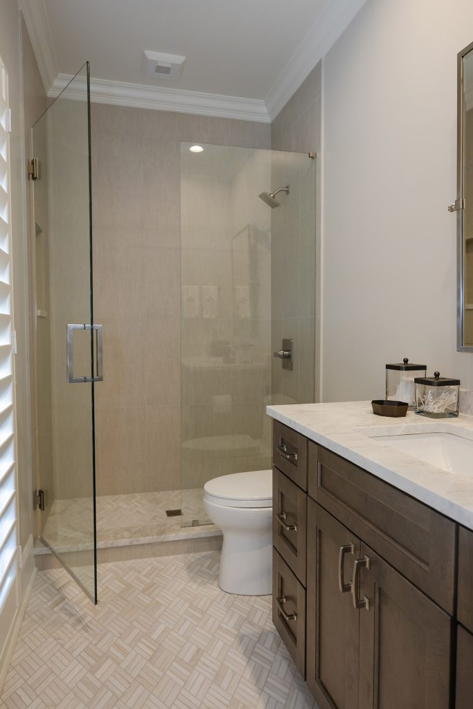 Guest bathroom with a glass shower, dark shaker vanity, marble-look counter, and herringbone tile floor.