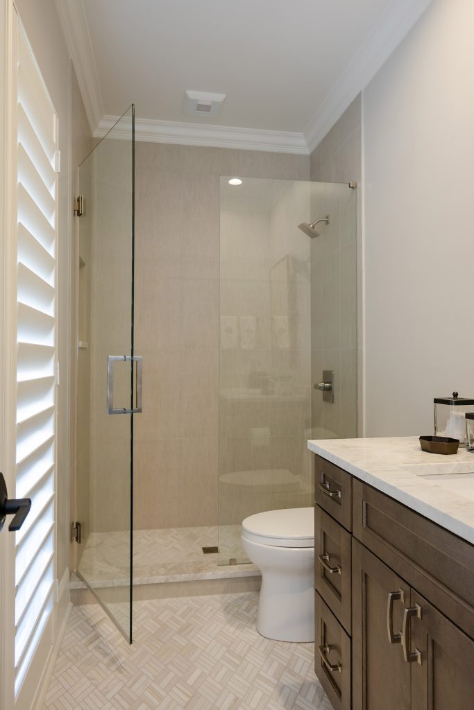 Guest bath with a frameless glass shower, greige large-format tile, and a dark vanity with a marble-look top.