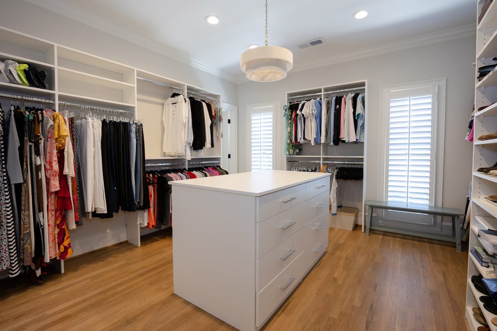 Custom walk-in closet with white shelving, hanging rods, a drawer island, and shuttered windows.