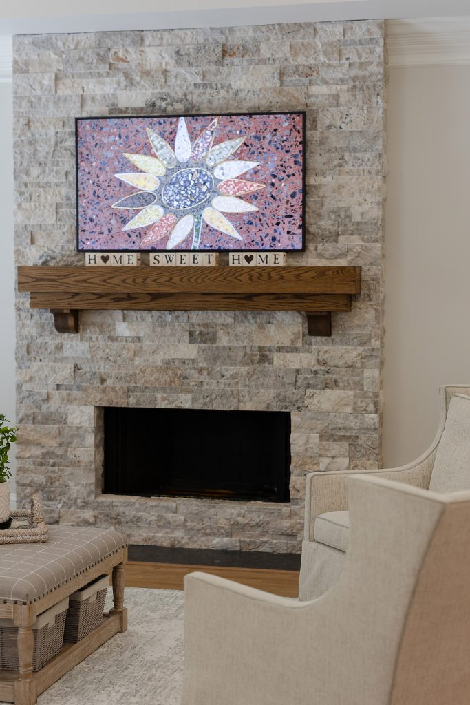 Stacked-stone fireplace with a terrazzo sunflower panel, stained-oak mantel, and cream upholstered chairs.
