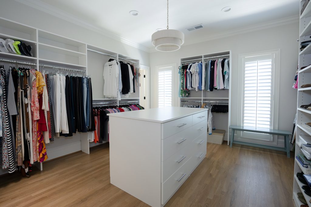 Walk-in closet with white built-in shelving, a center island of drawers, and a drum pendant over wood floors.